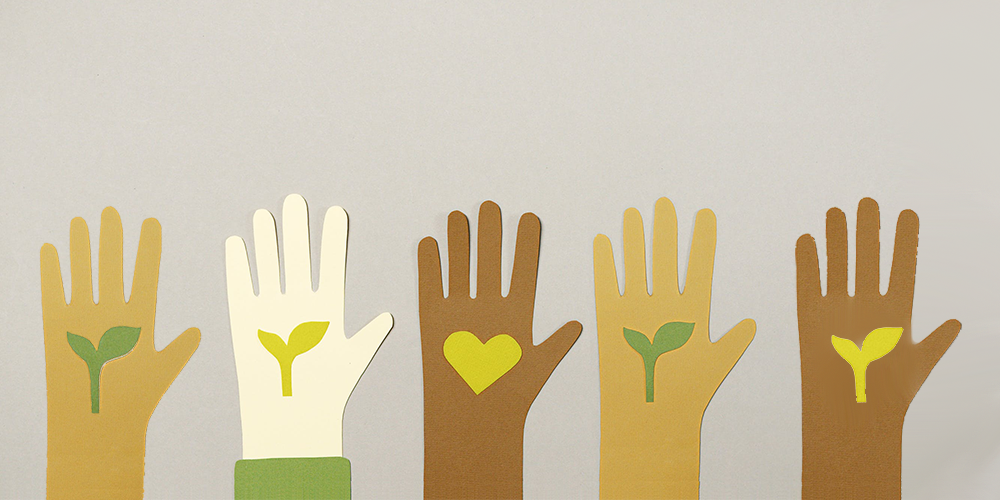 5 hands (made out of small cut out paper) in different shades of skin color: from dark to light hold up five fingers each. The four hands on either side of the frame have a budding leaf in their palms. The hand at the center has a heart in its palm. 