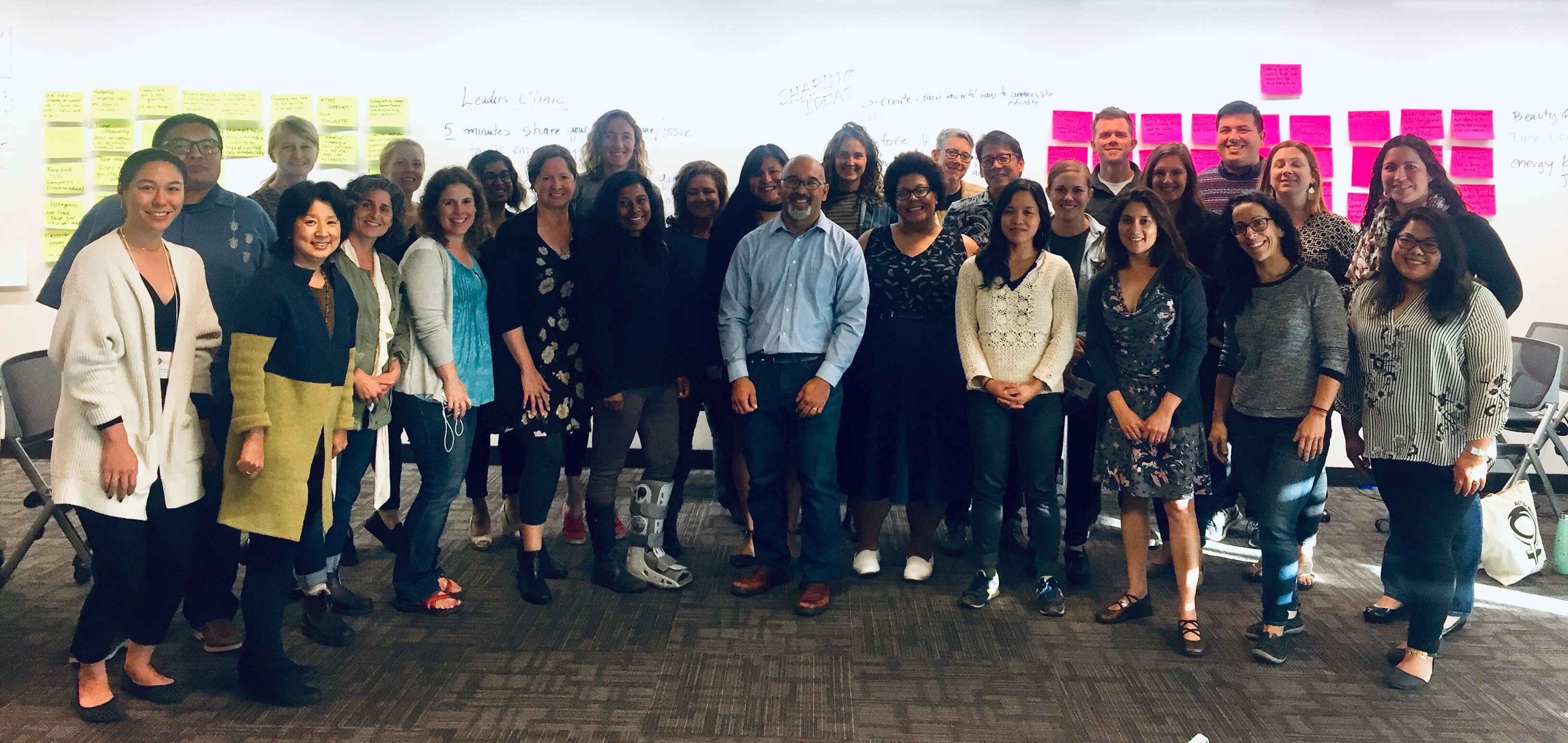 The 2018 Fundraising Bright Spots cohort stands smiling in front of a dry erase board with lots of colorful sticky notes on it.