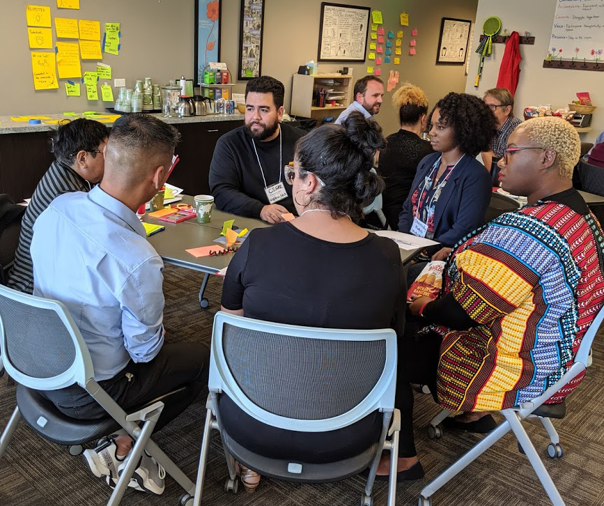 A diverse group of CompassPoint workshop participants sit around a table working together. 