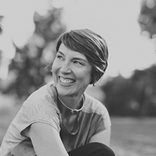 A black and white image of Rebecca: a white woman with not-quite-dark-hair who is smiling and looking off to the side