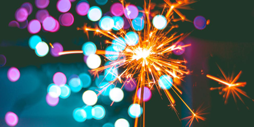 A bright, beautiful sparkler lights up the dark with orange embers and flashes of purple and blue light. 